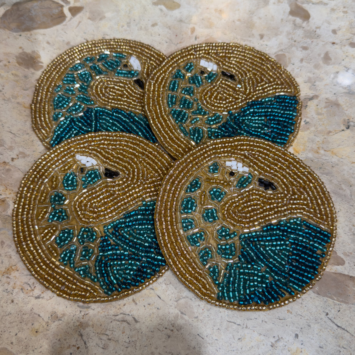 Four ornate circular beaded gold coasters with gold peacocks.