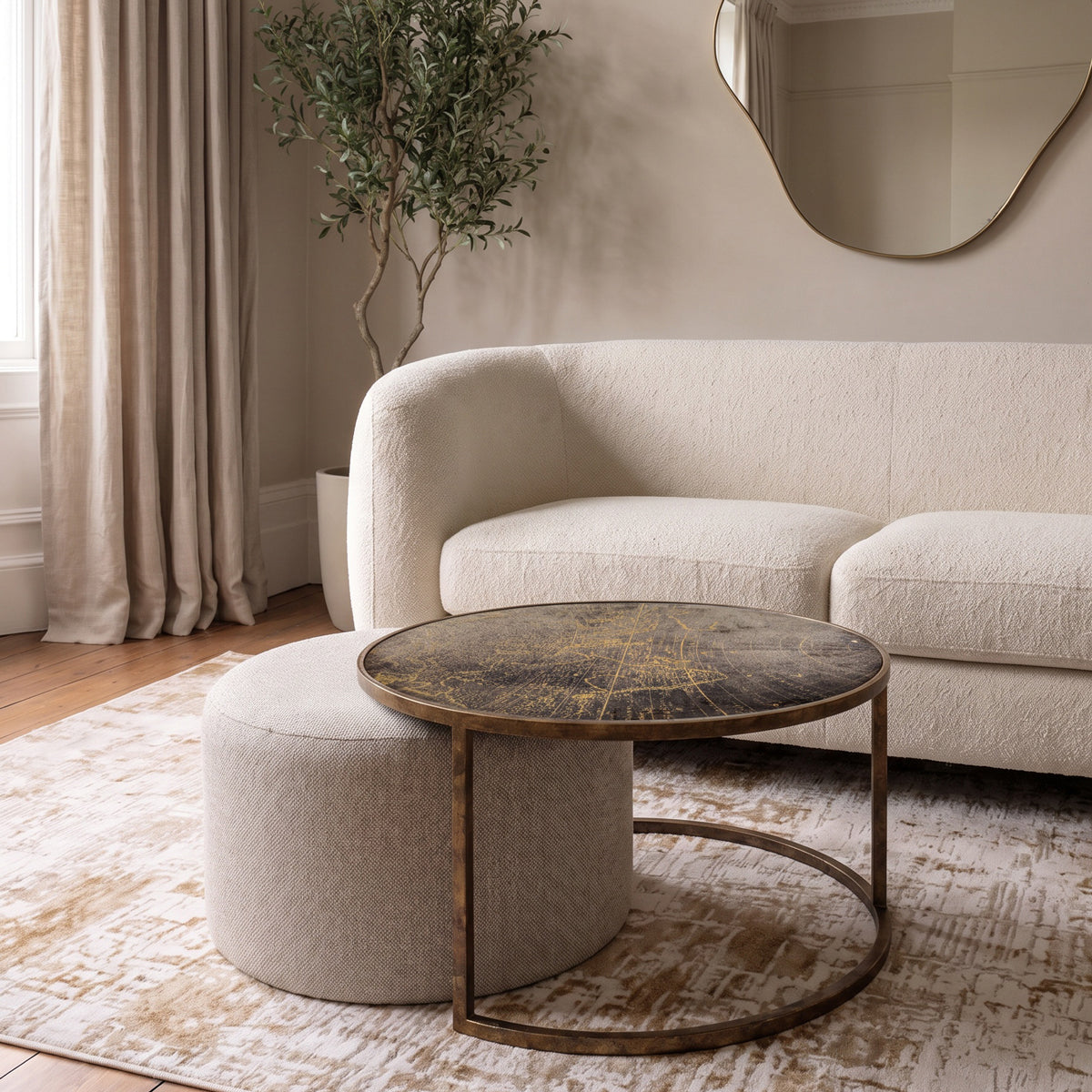 A round coffee table with a map motif top and brass metal frame, styled in a modern living room next to a cream bouclé sofa.