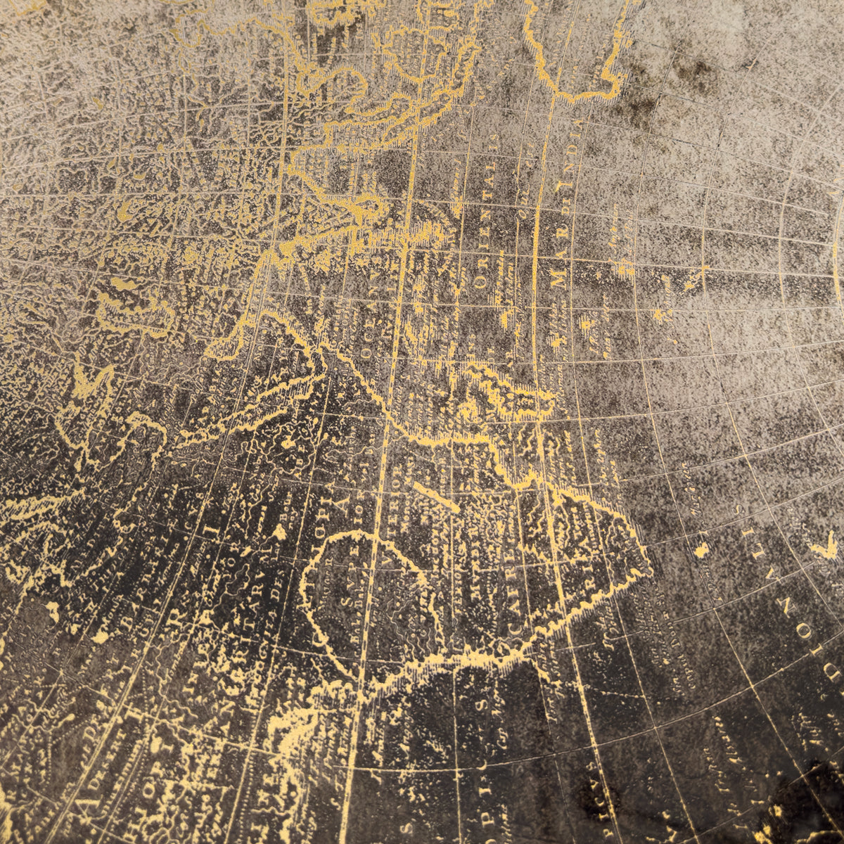 Close-up of an antique-style map pattern with gold linework and text on a dark textured background.