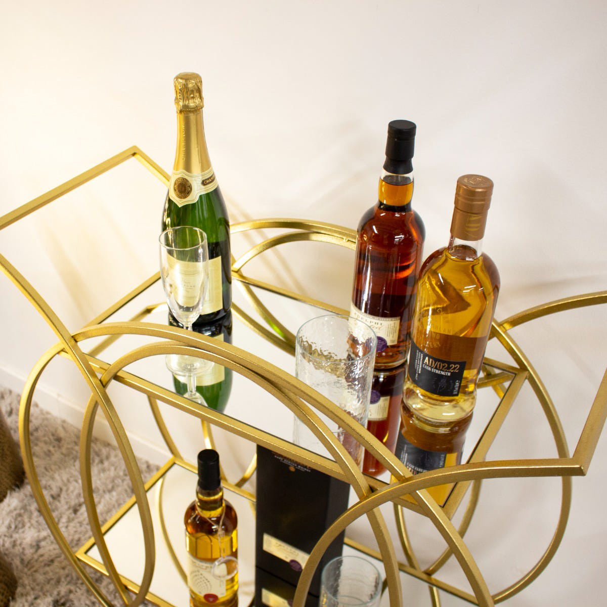 Gold bar cart with wine bottles and glasses on a white background