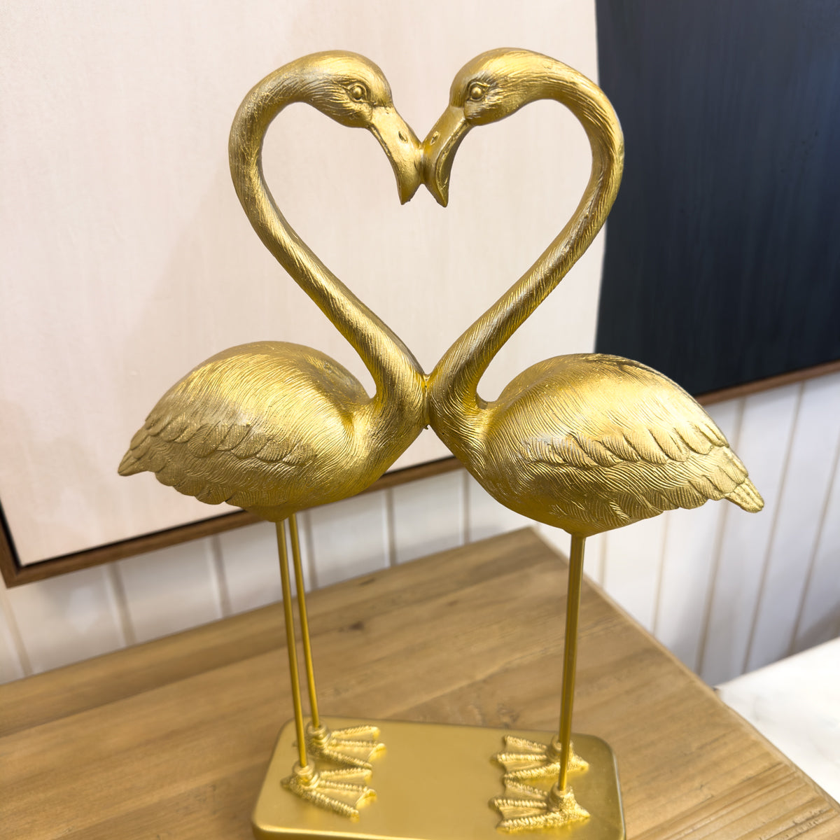 Gold flamingo statue forming a heart shape on a wooden surface.