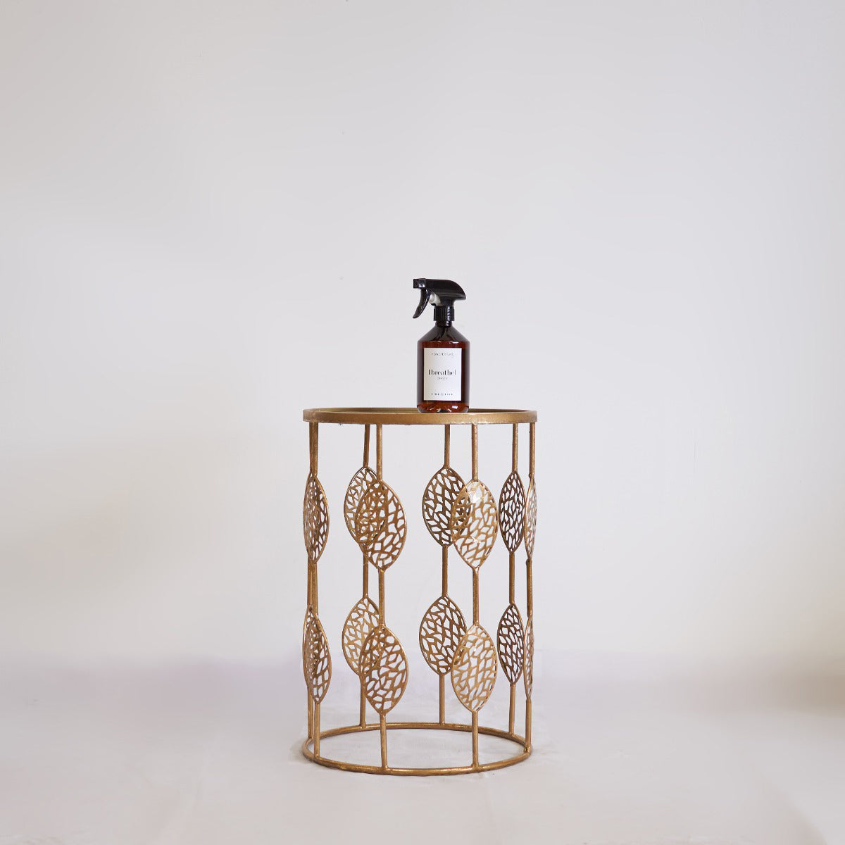 Decorative metal side table with a bottle on a plain background