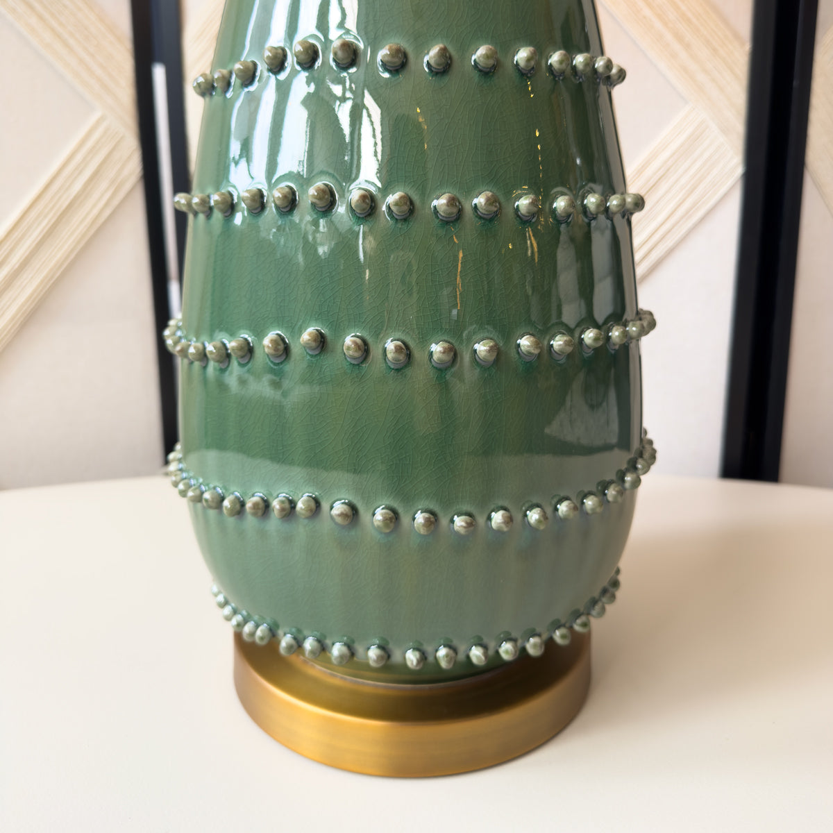 A close up of a green bobble table lamp with a golden base