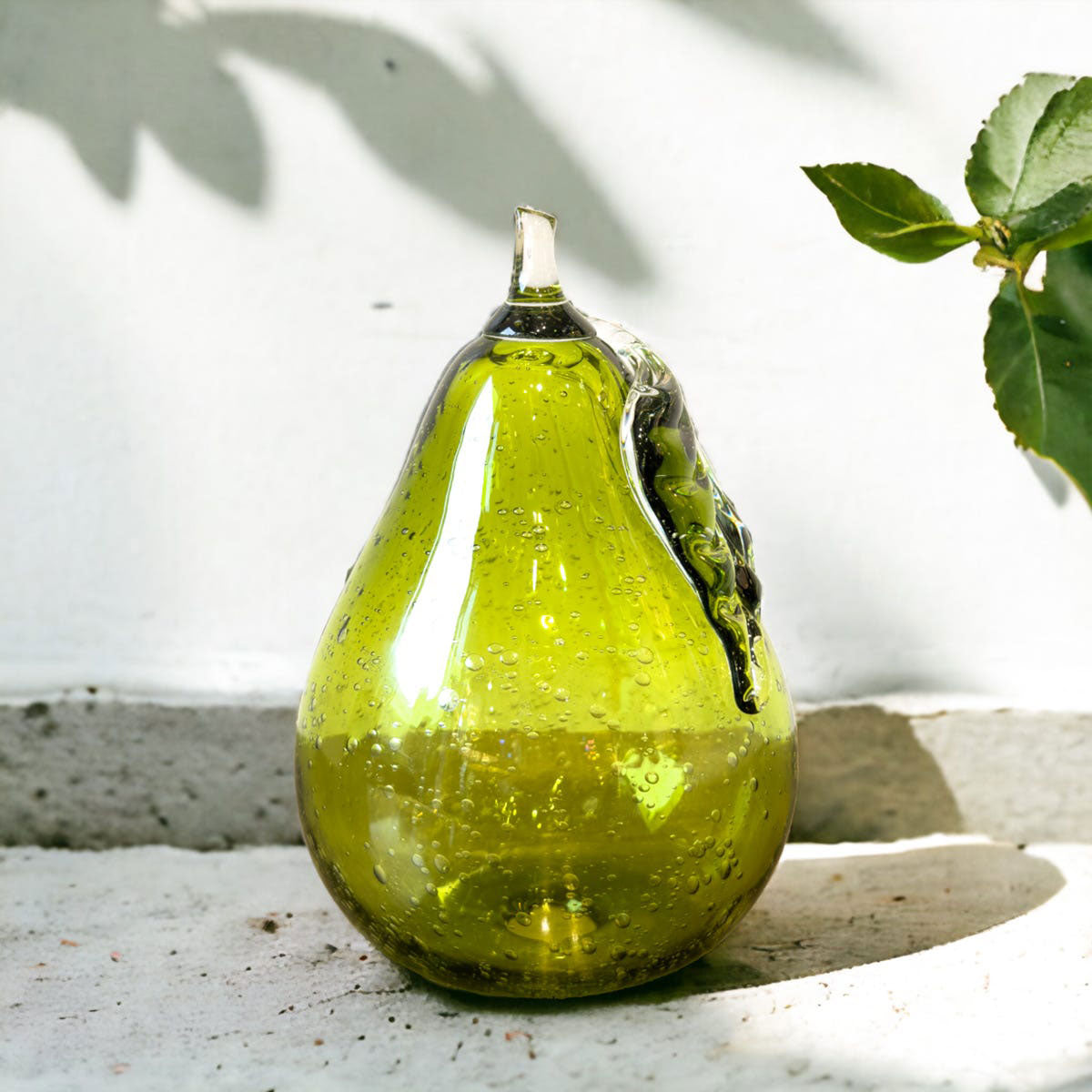 Green glass pear-shaped object on a light surface with leaves in the background