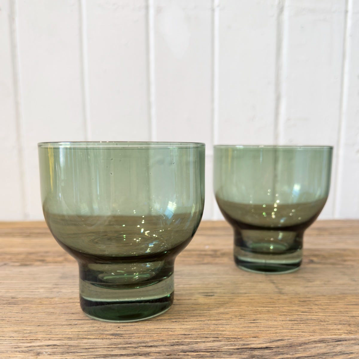 Two olive green glass tumblers with a curved design, placed on a wooden surface.