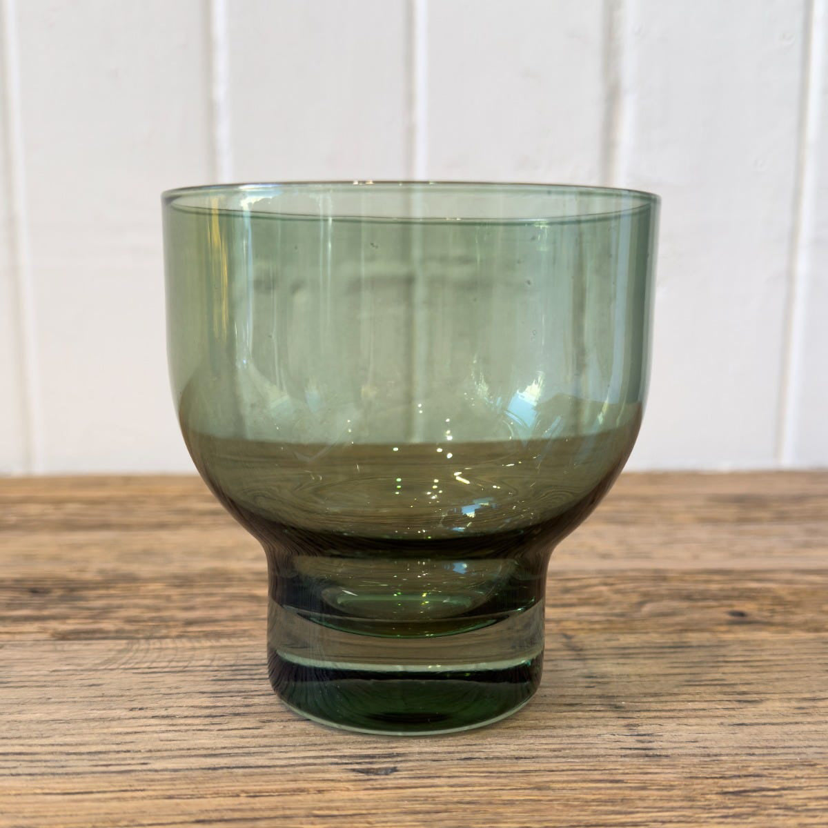 Green glass tumbler on a wooden surface with a white paneled background