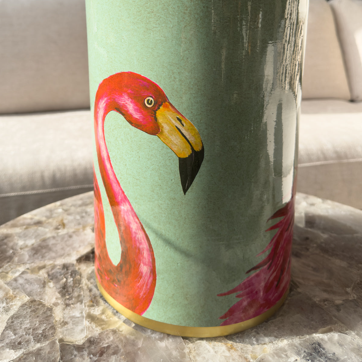 A close up of a green ginger jar with flamingo pattern, sitting on a quartz coffee table.