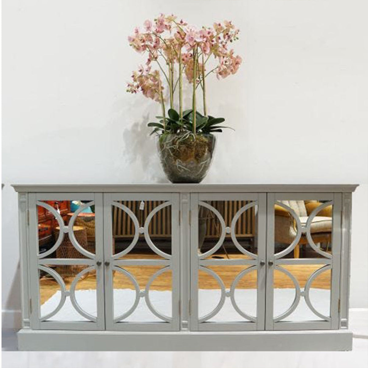 Grey sideboard with decorative mirror panels and a pink orchid in a clear vase on a white background