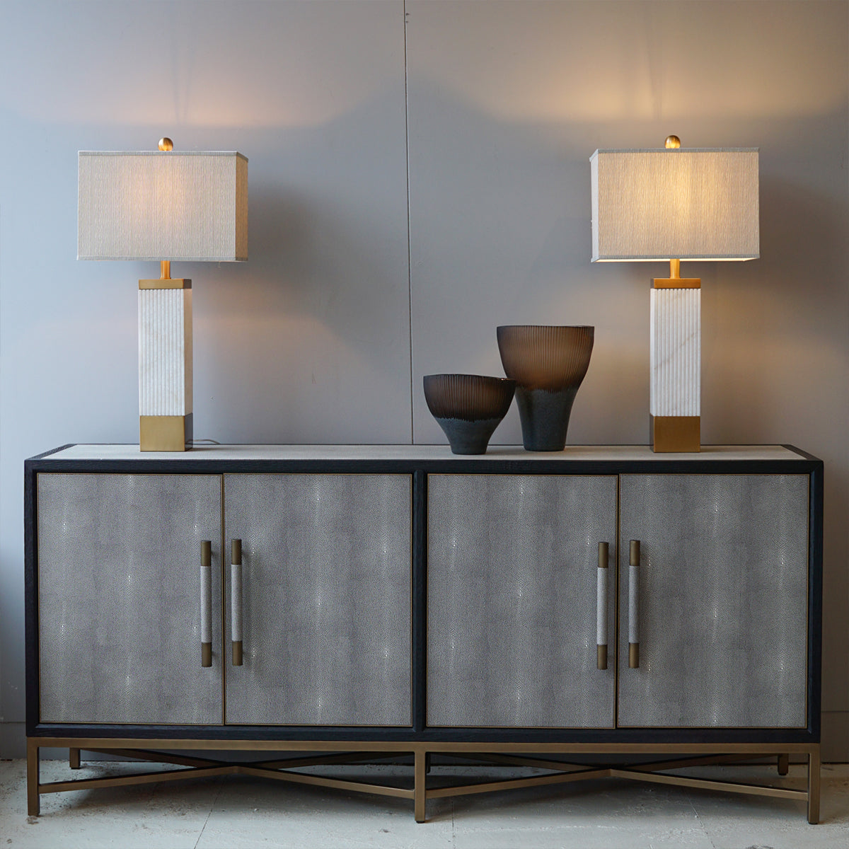 Two lamps on a sideboard with decorative bowls against a plain wall.