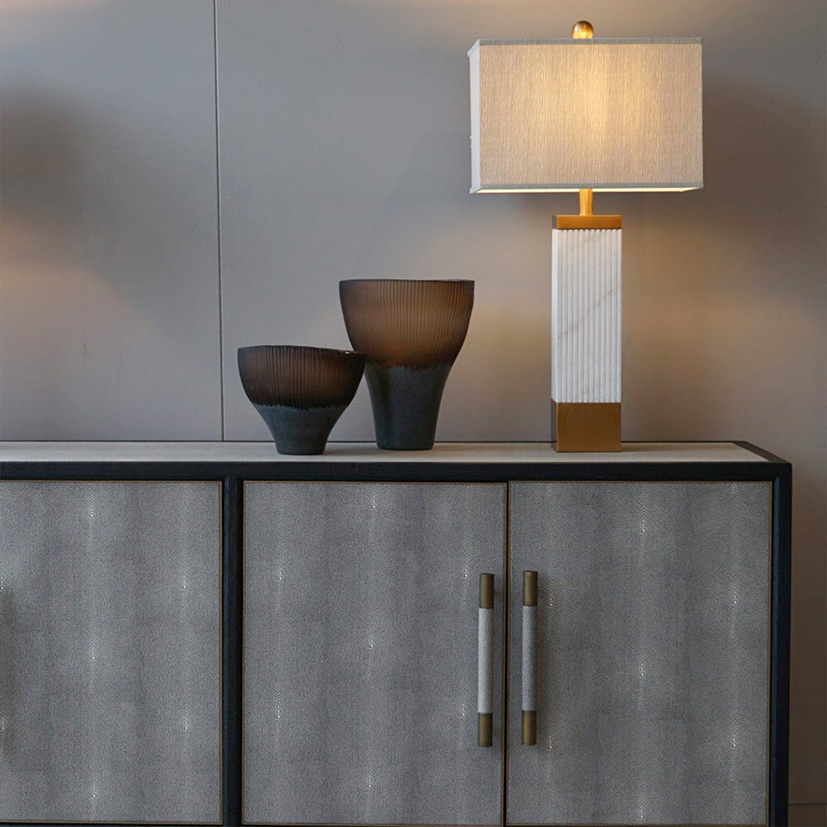 Decorative lamp and bowls on a monochrome shagreen cabinet against a neutral wall.