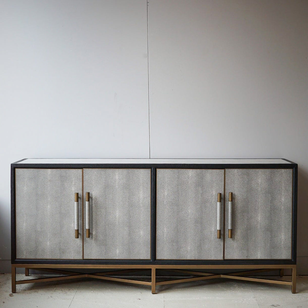 Modern shagreen cabinet with textured doors and gold handles against a plain wall.