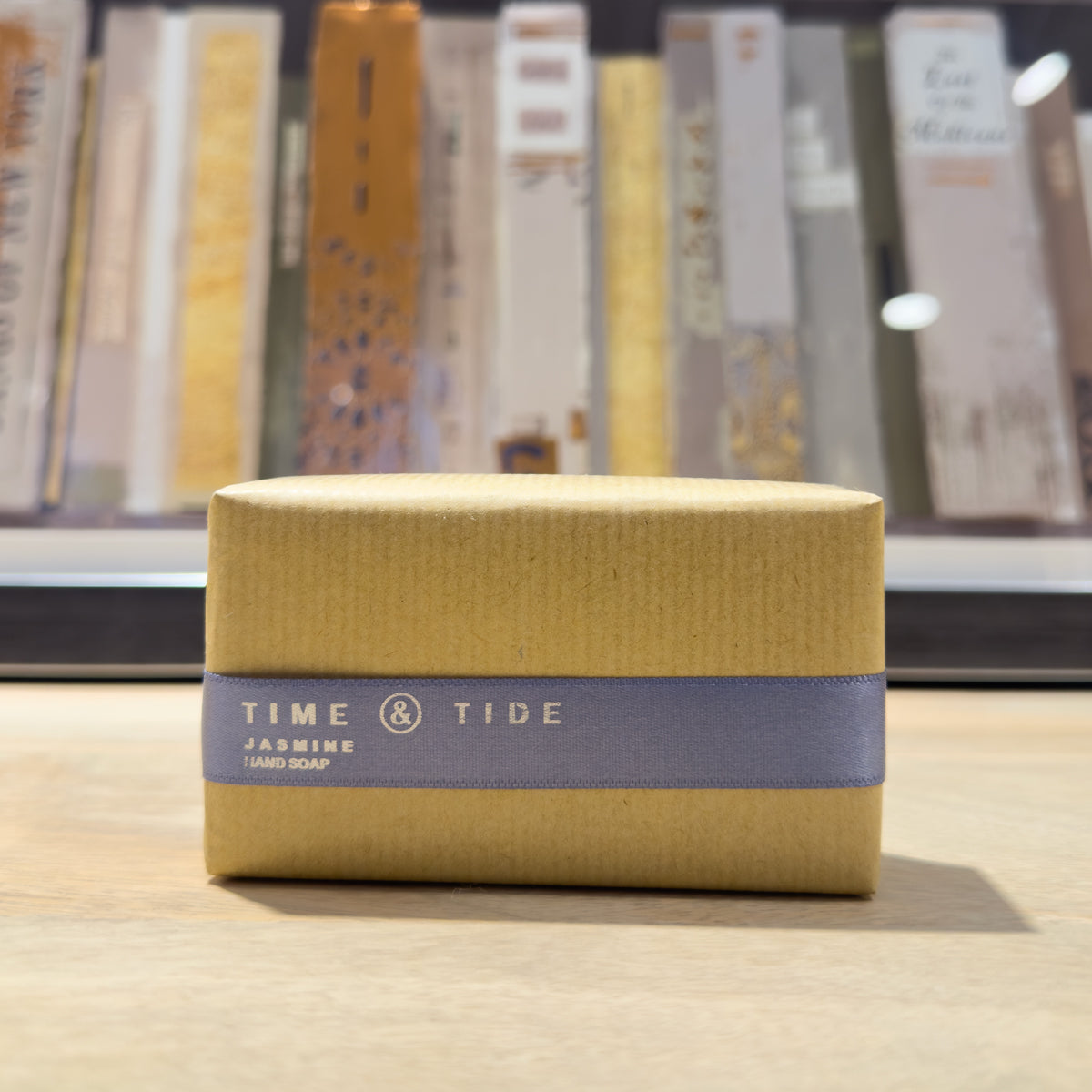 Bar of jasmine soap with 'Time & Tide' branding on a wooden surface with books artwork in the background