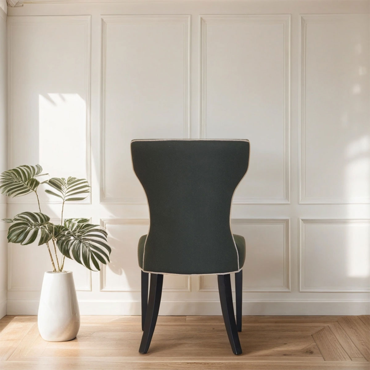 Dark green chair in a room with white paneled walls and a plant on a wooden floor.