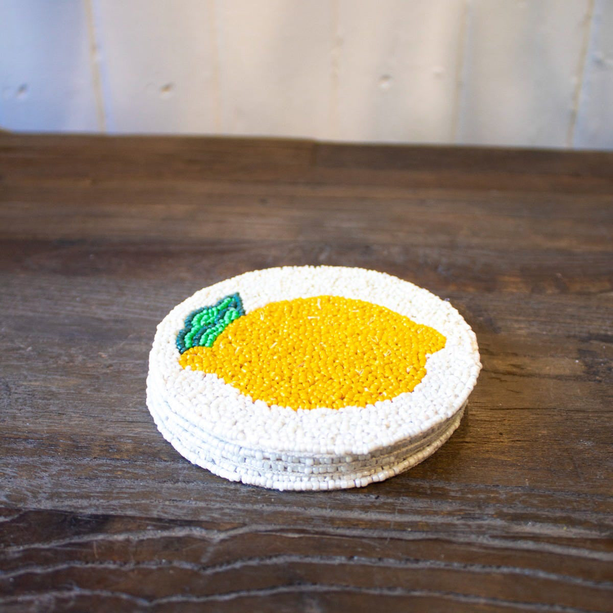 Stack of round coasters with a lemon design on a wooden surface