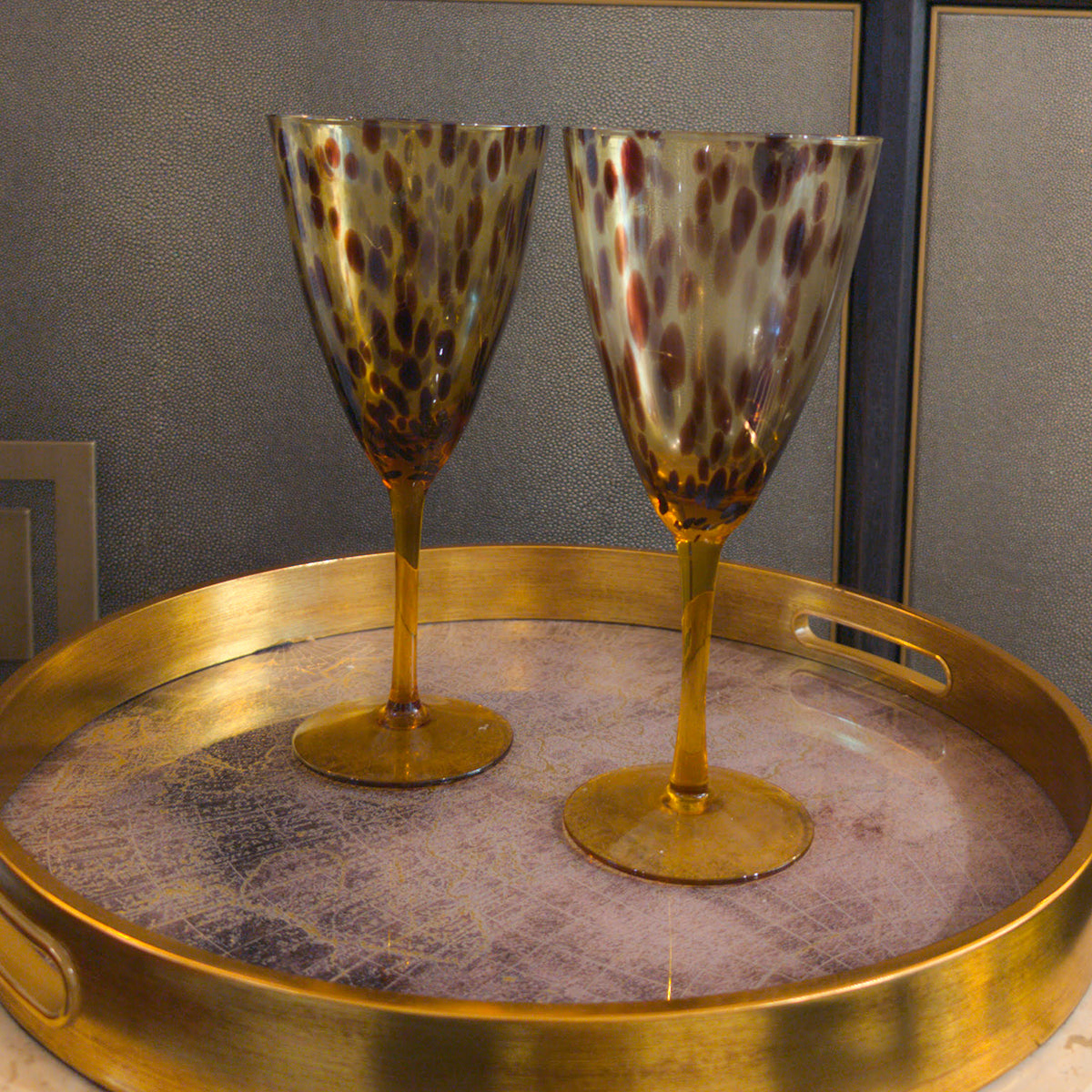 Two leopard print wine glasses on a gold tray with a gray background