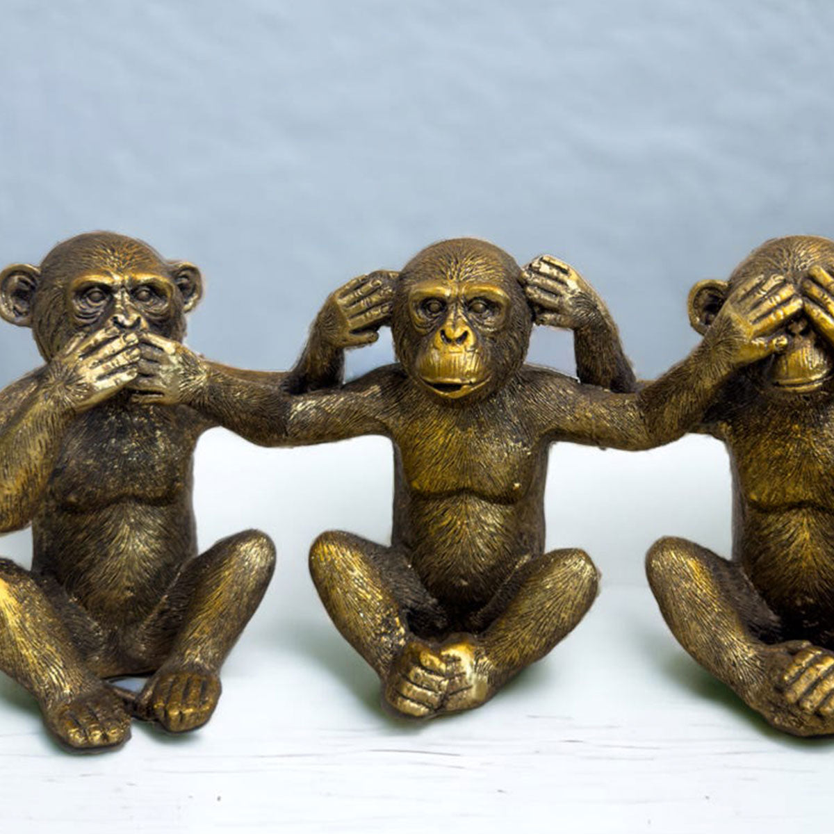 Three bronze monkey figurines representing 'see no evil, hear no evil, speak no evil' on a light gray background.