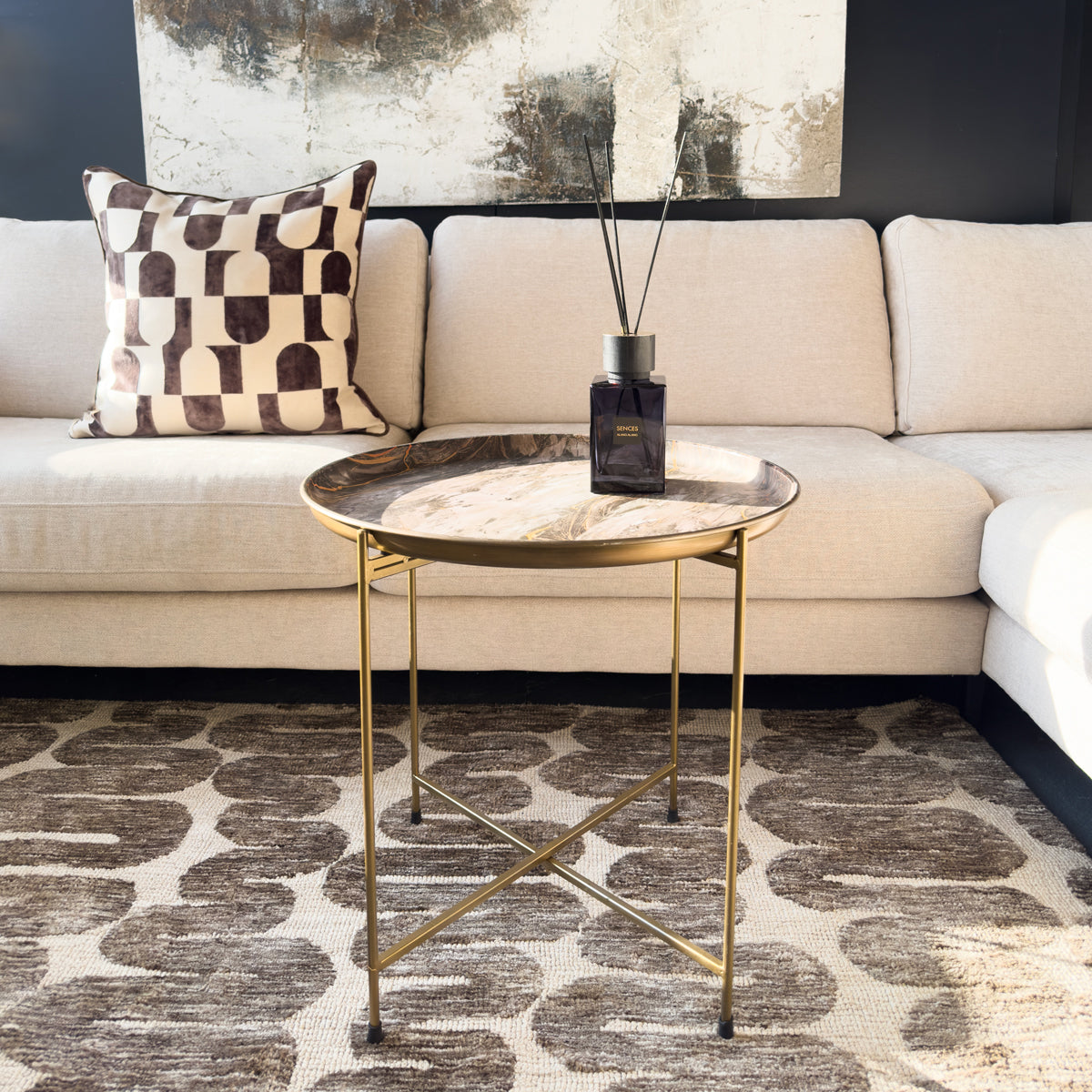 Modern living room with a beige sectional sofa, gold side table, and abstract painting.