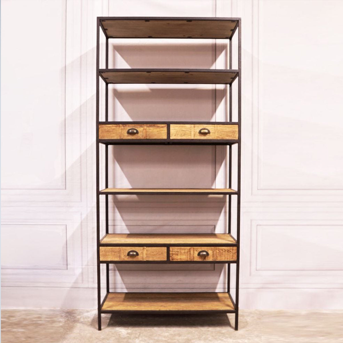 Tall bookshelf with wooden shelves and drawers against a white wall.