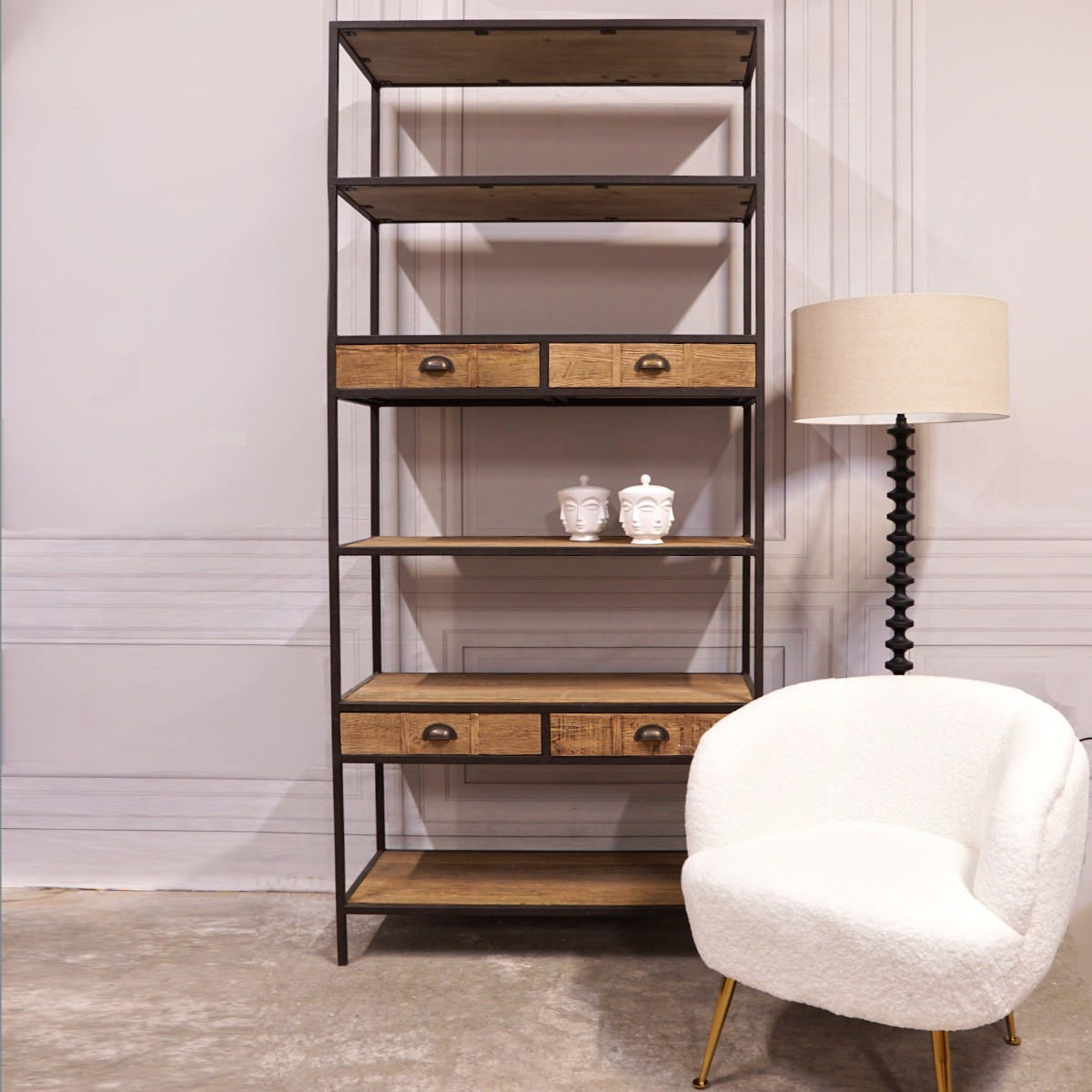 Wooden shelf with drawers and shelves in a room with a white chair and lamp.