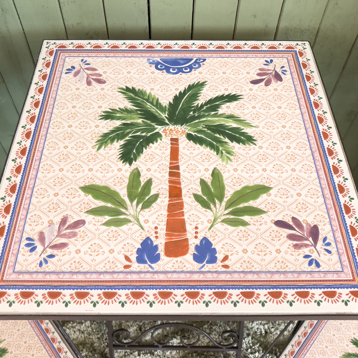 Decorative patterned table with a palm tree design against a wooden slatted wall.
