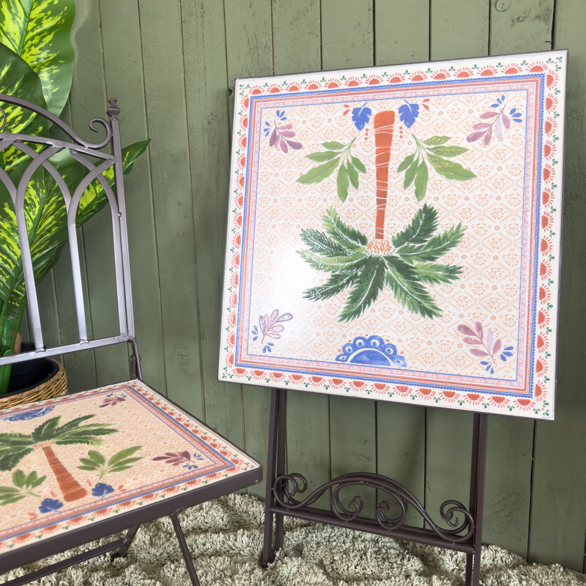 Decorative foldable table and chair set with floral and palm patterns against a green wooden wall.