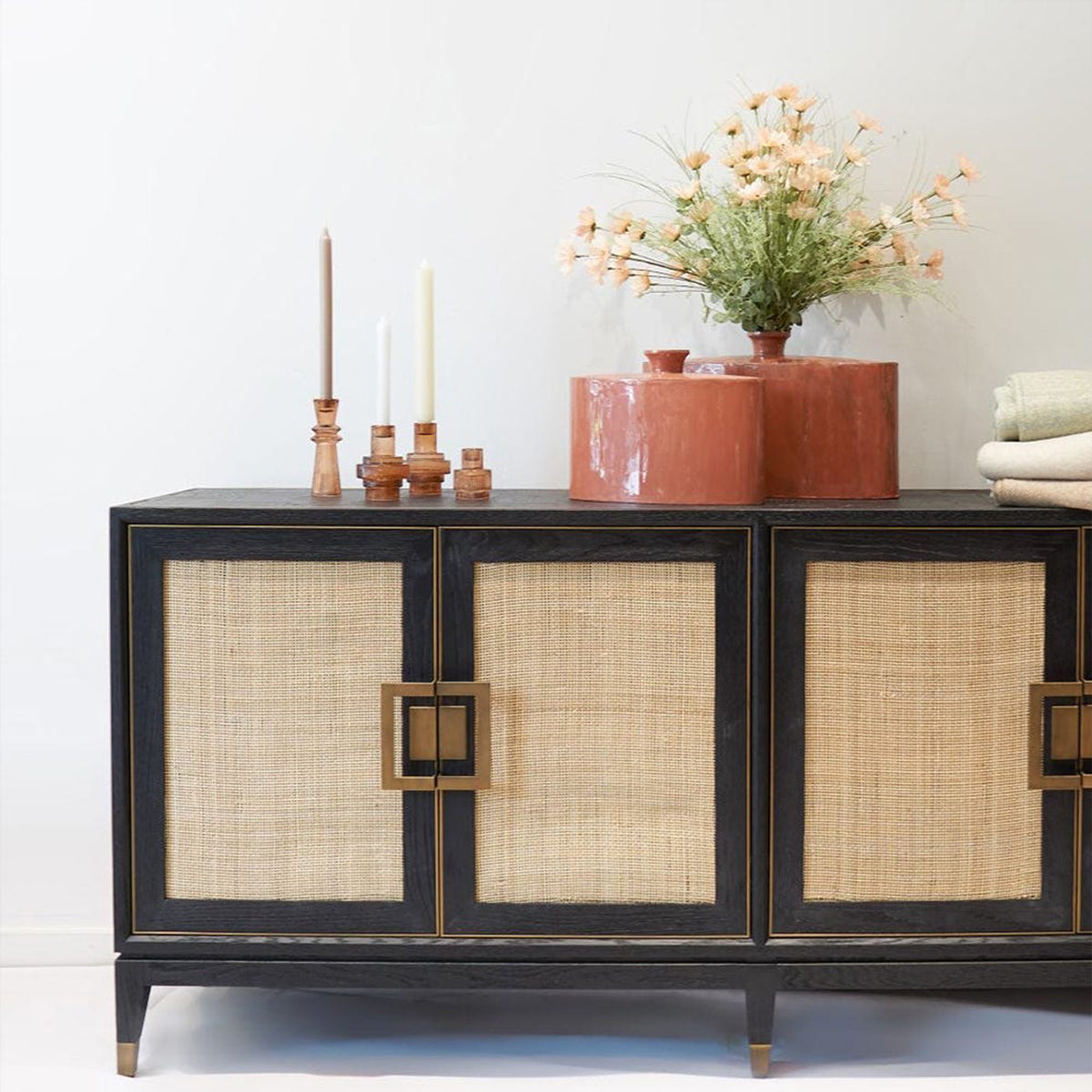 Decorative sideboard with rattan doors and gold accents, featuring candles and a plant on a white background.