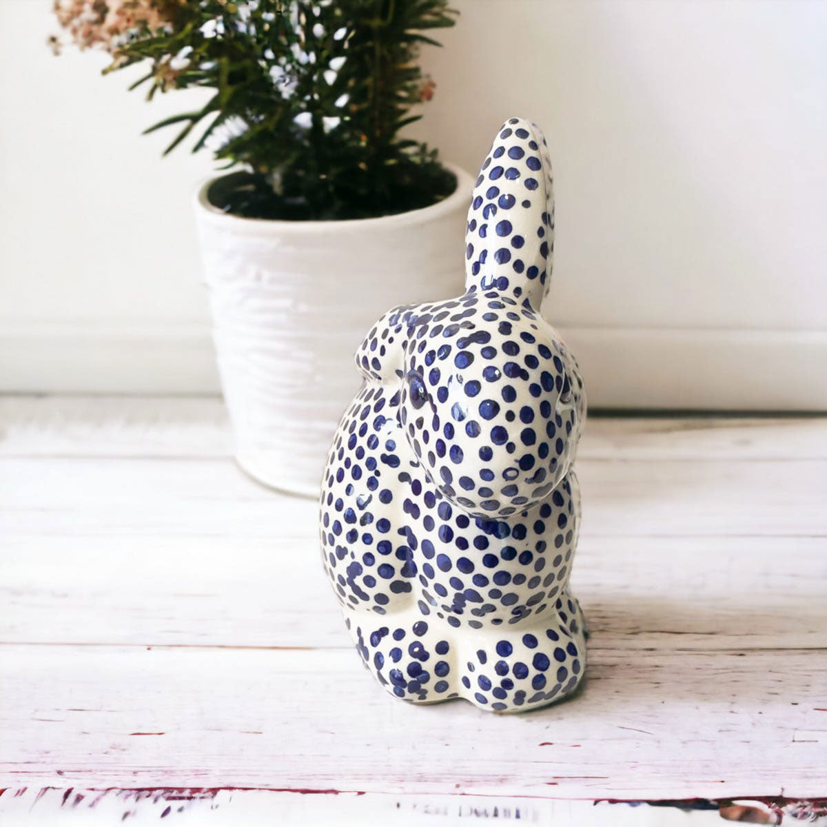 Ceramic rabbit figurine with blue polka dots on a white wooden surface with a plant in the background.