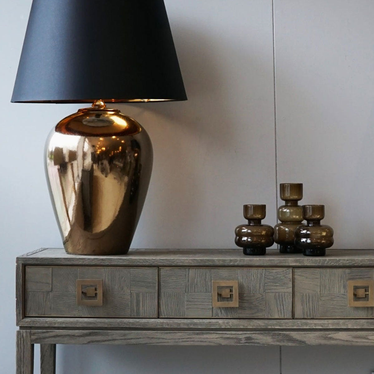 Bronze lamp on a wooden console table with decorative vases against a light wall.