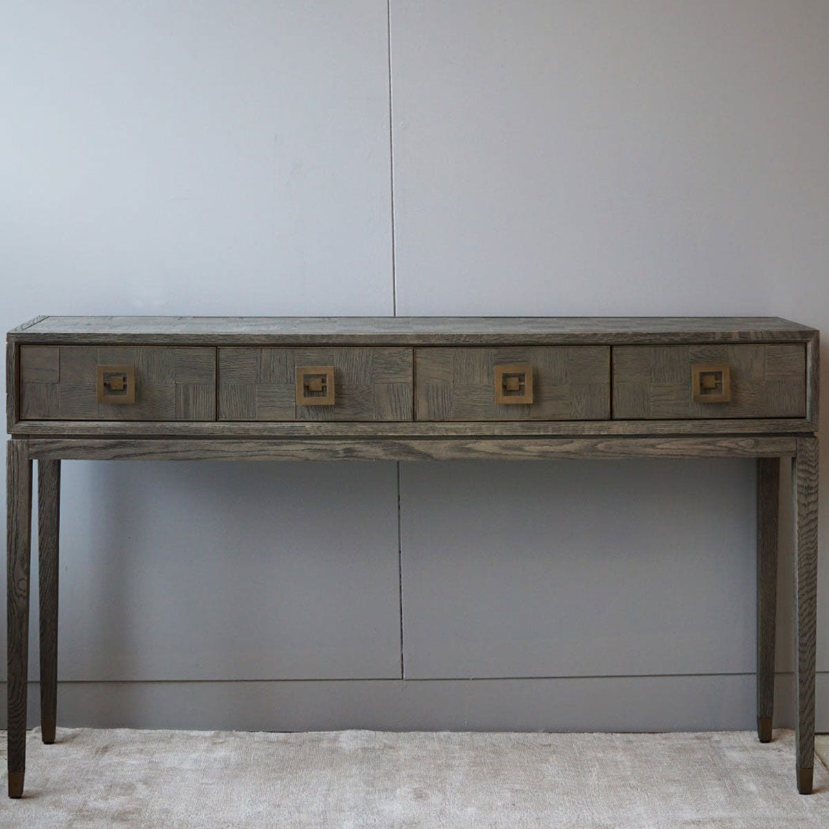 Wooden parquet console table with four drawers against a plain wall