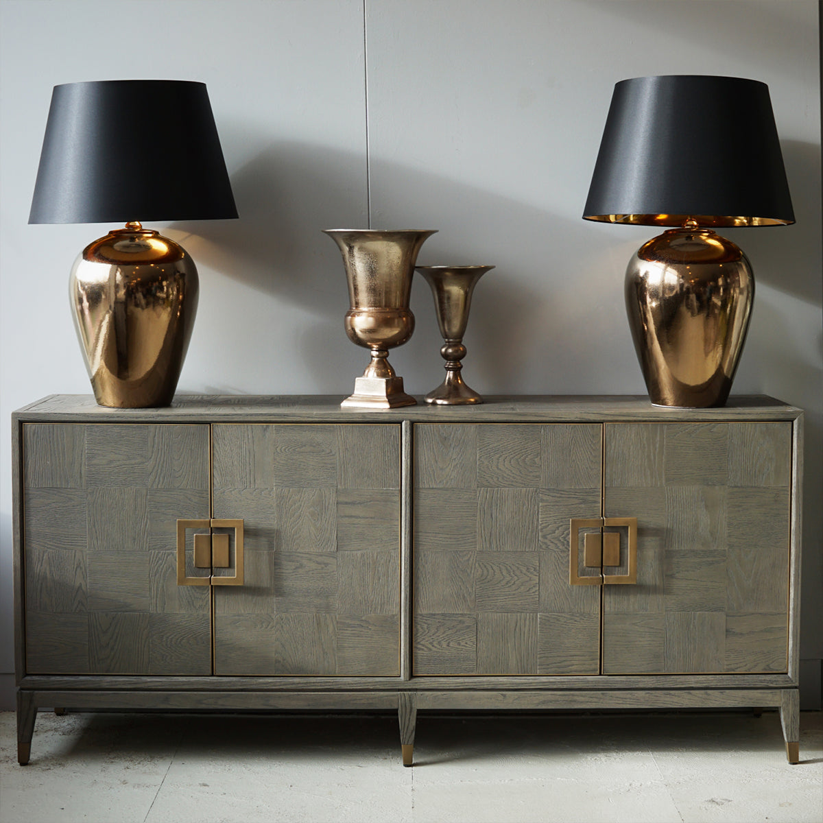 Decorative sideboard with two gold lamps and two decorative urns on a plain background