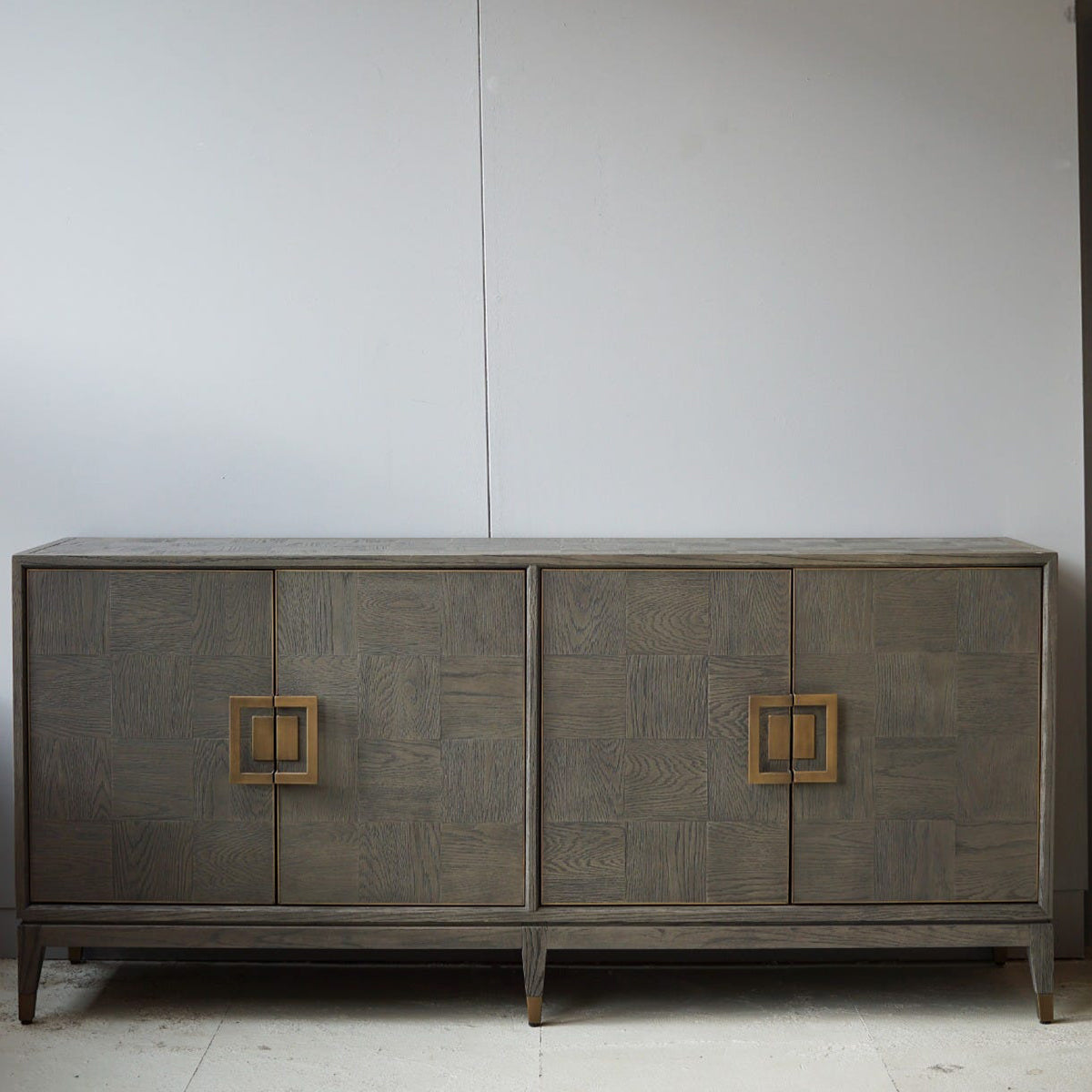 Wooden parquet sideboard with square handles against a plain wall