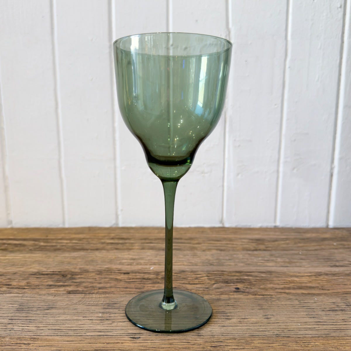 Green wine glass on a wooden surface with a white paneled background