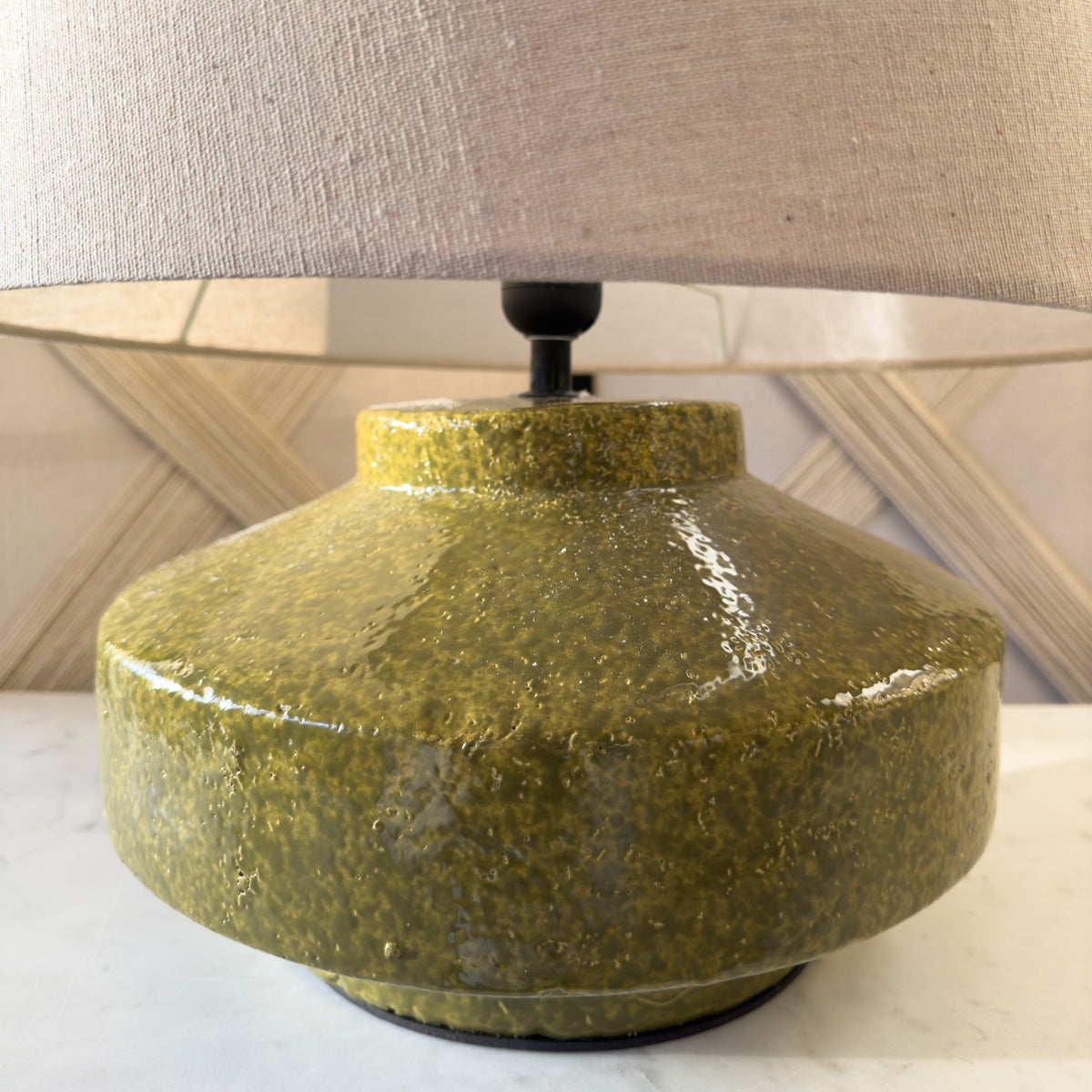 A close up of a green table lamp with a disc shaped base and beige linen shade.