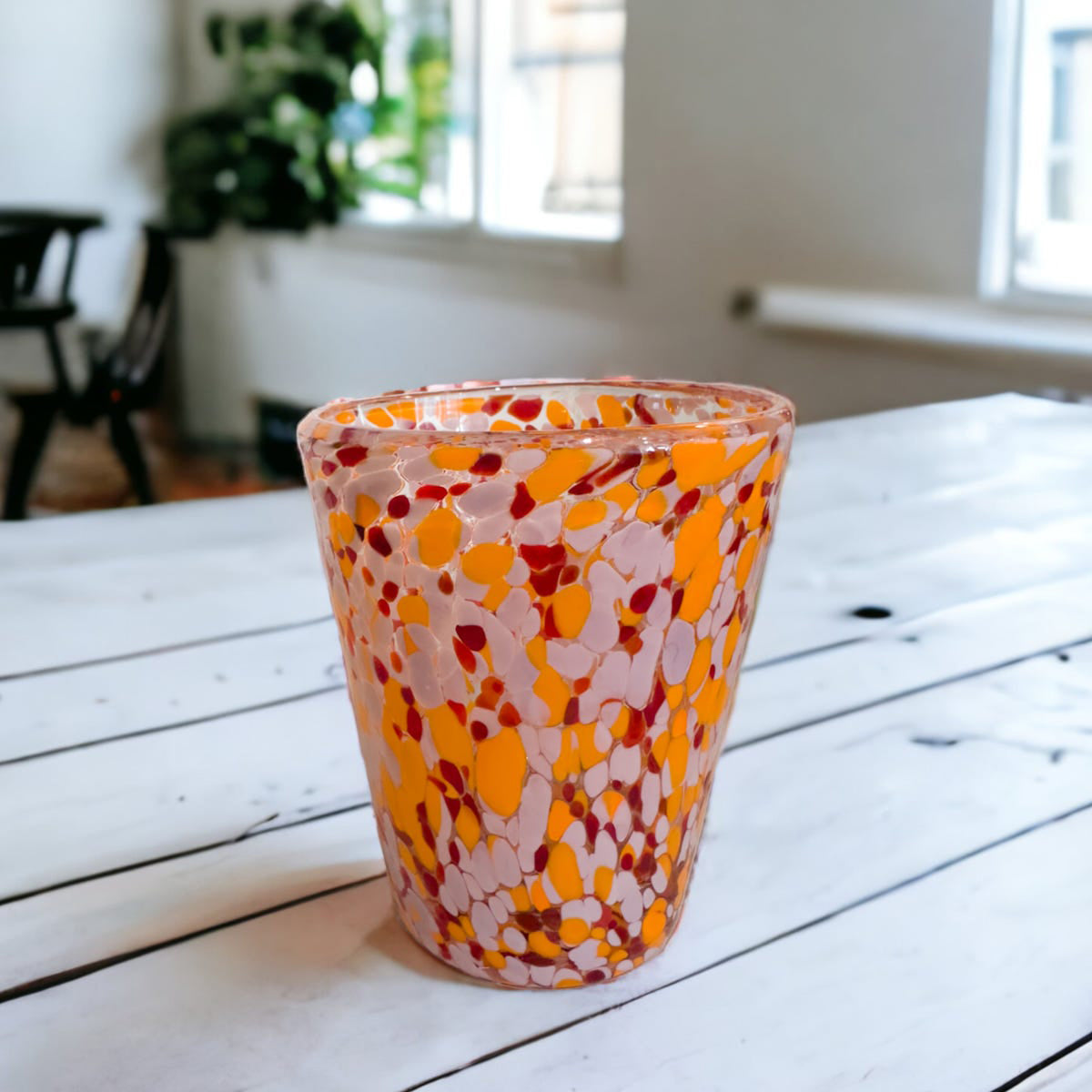 A pink and orange confetti pattern tumbler on a white wooden table.