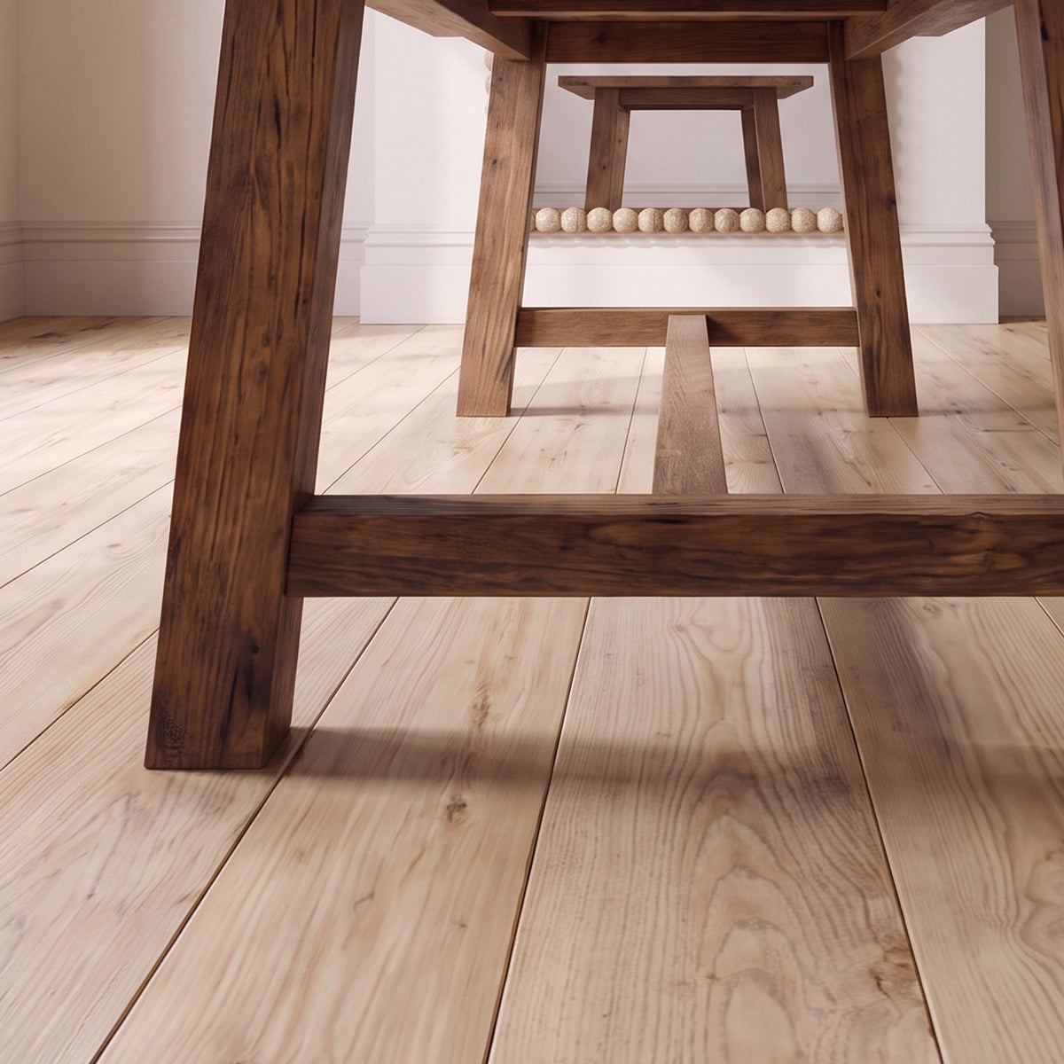 Light natural wood plank flooring shown from a low angle beneath a dark wooden table against a neutral wall.