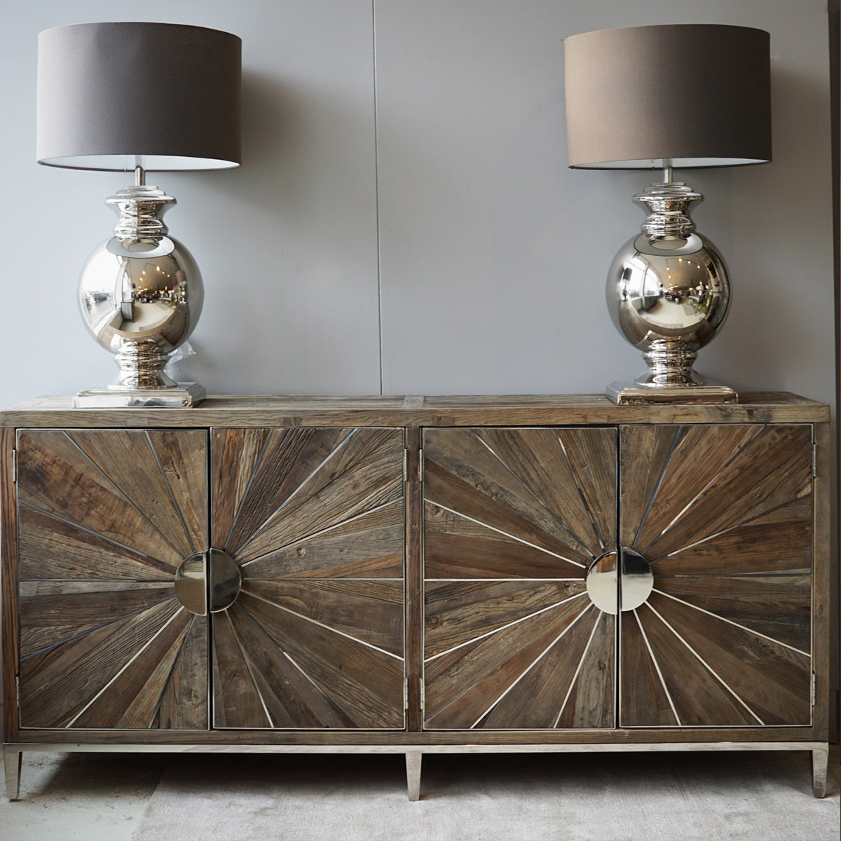 Wooden sideboard with decorative sunburst pattern and two matching lamps on a neutral background