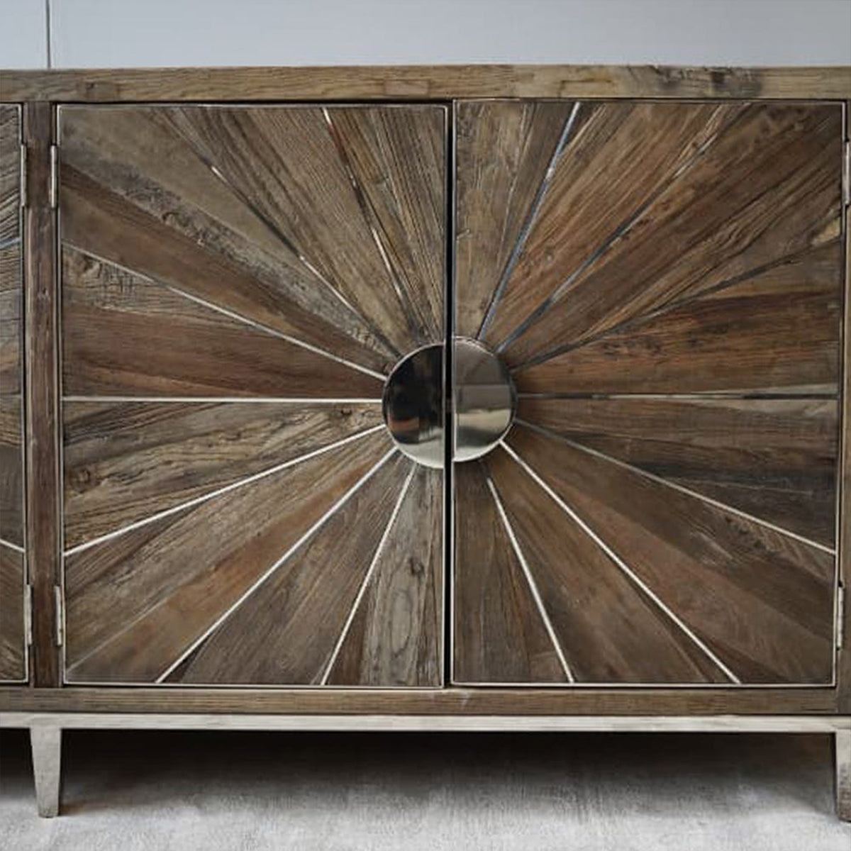 Wooden cabinet with sunburst design and metallic center on a neutral background