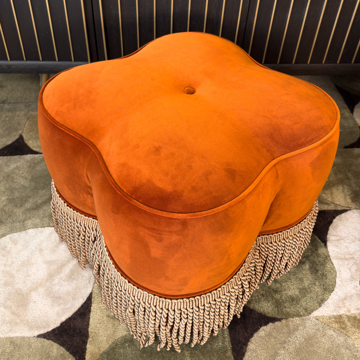 Orange ottoman with fringe on a patterned rug