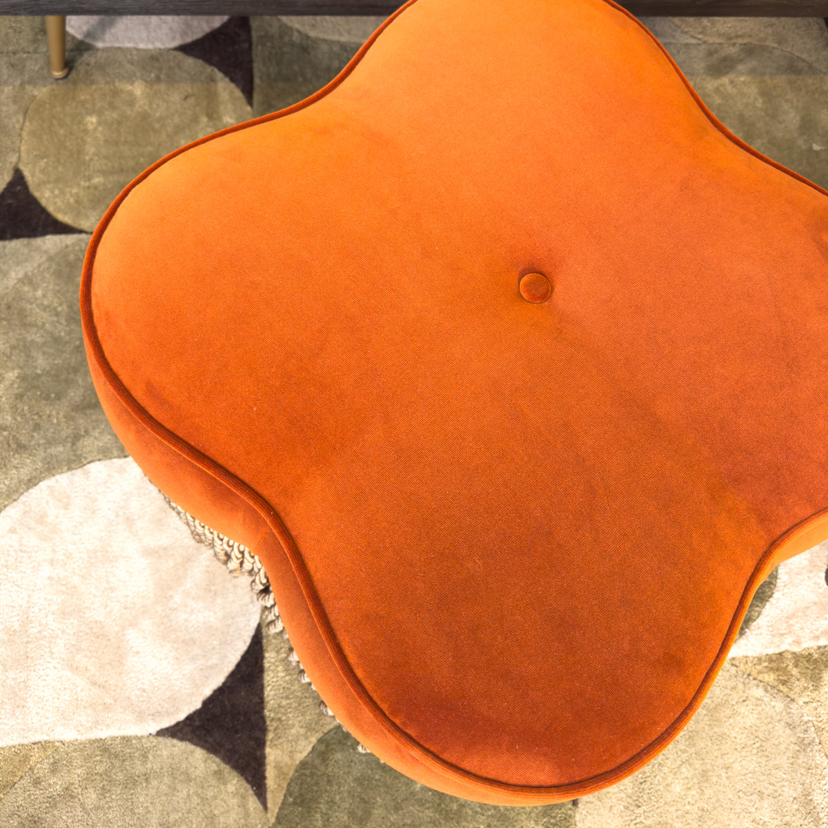 Close-up of an orange footstool on a patterned green rug surface