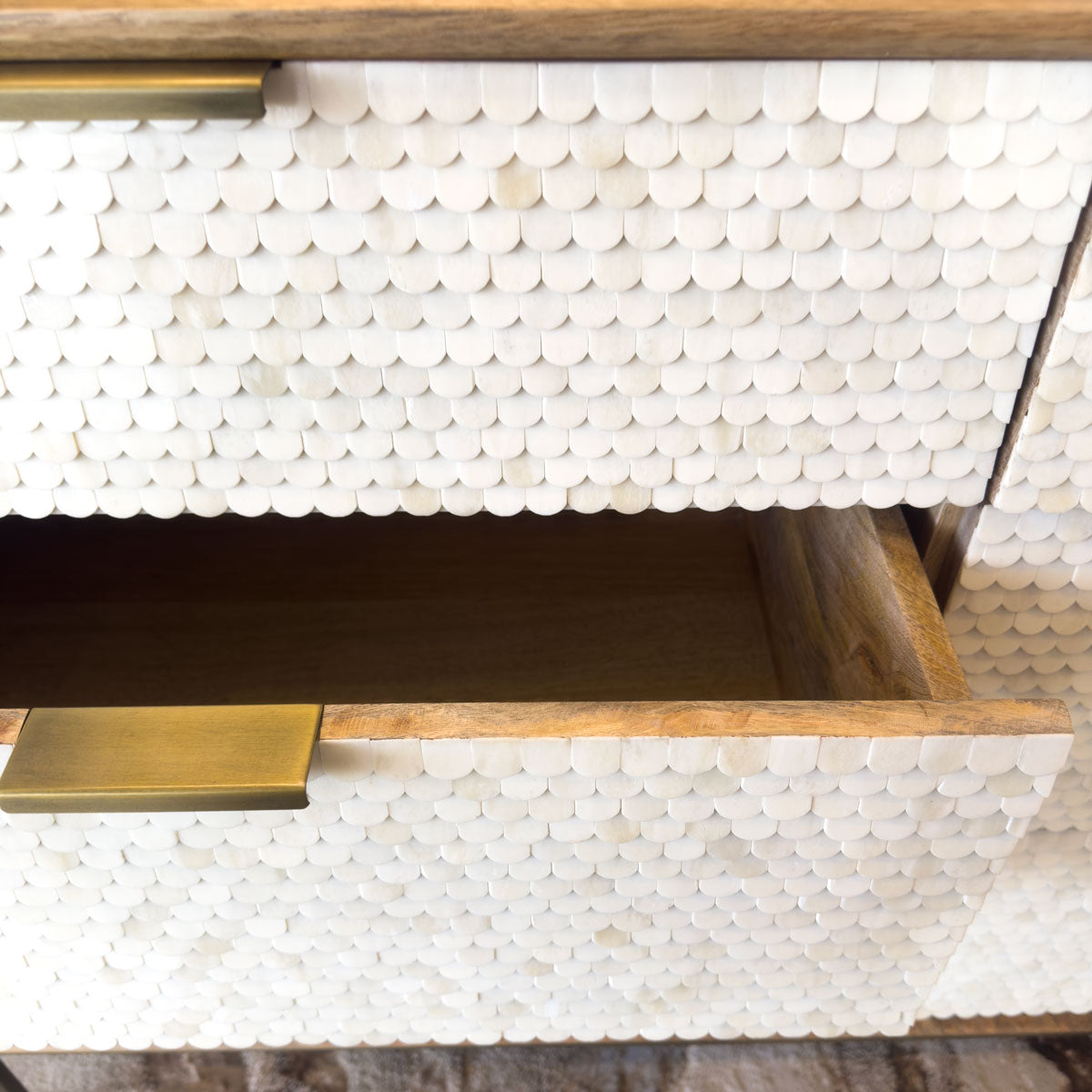 Close-up of a wooden dresser with white shell-patterned inlay and brass handles.