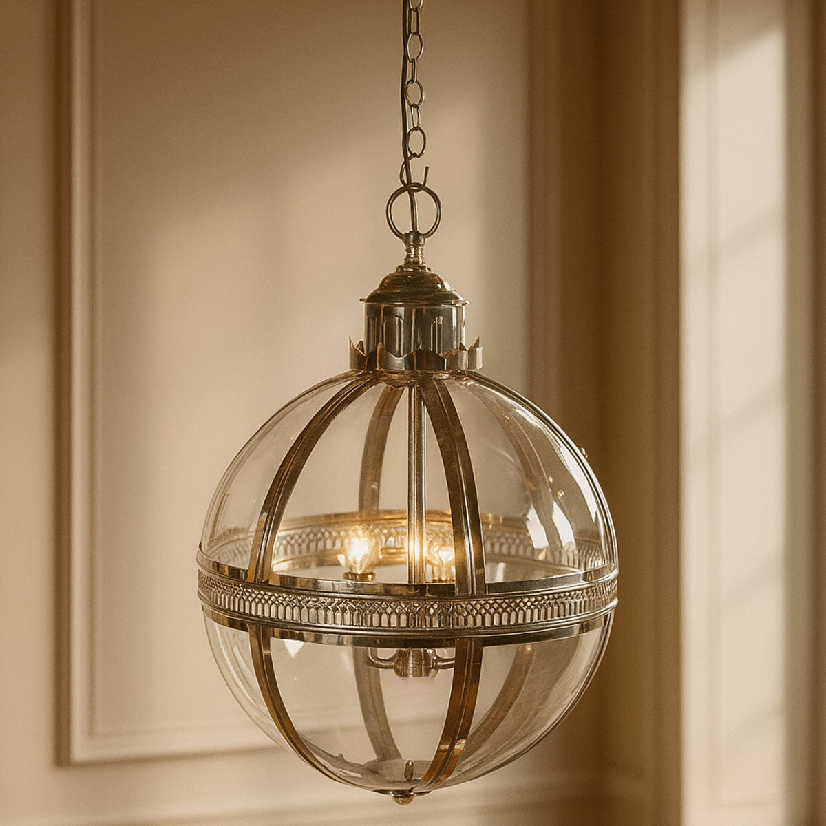 Decorative pendant light with clear glass sphere and metallic frame hanging against a neutral wall.