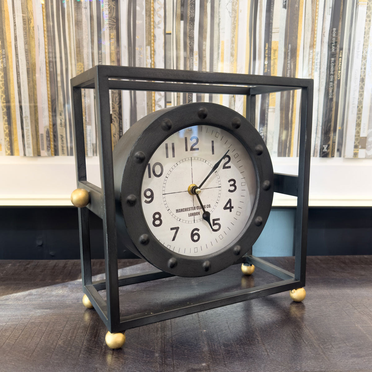 Decorative clock with black frame and white face on a wooden surface.