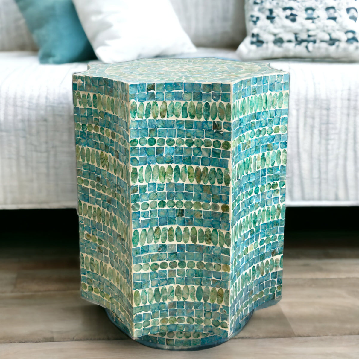 Hexagonal mosaic side table with green and blue tiles in front of a white sofa with patterned cushions.
