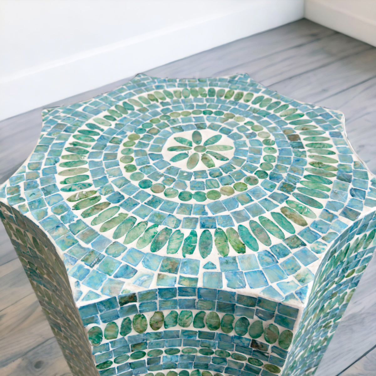 Hexagonal mosaic table with green and blue tiles on a wooden floor.