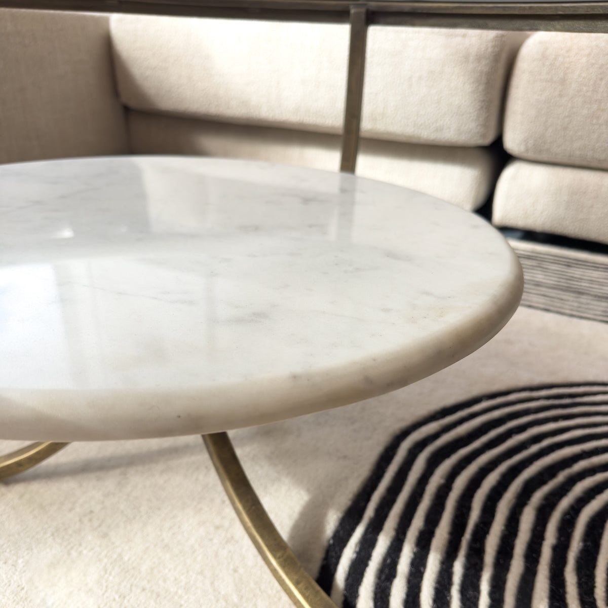 Round marble coffee table with gold legs in a living room setting.