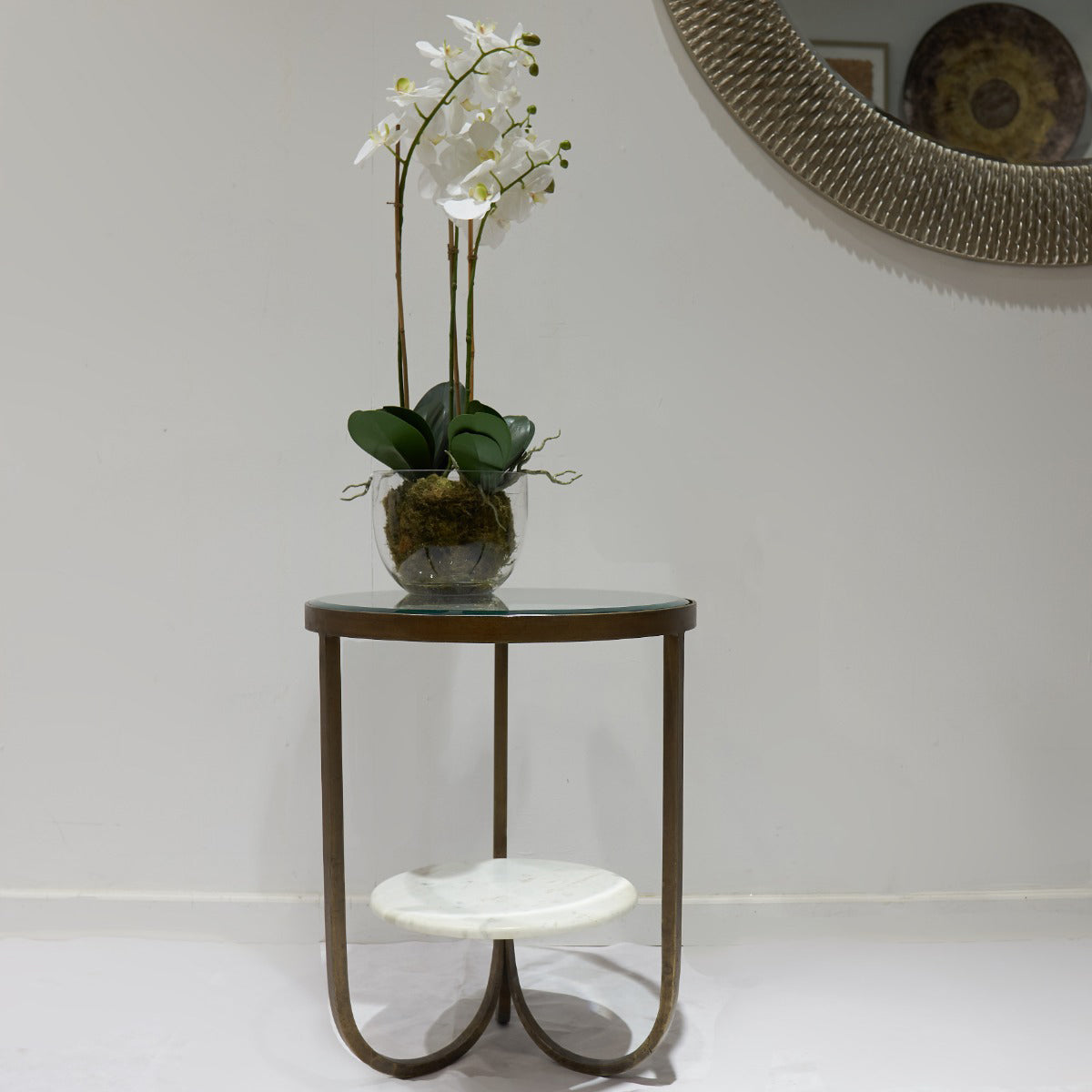 Small round table with a vase of white flowers against a plain wall.