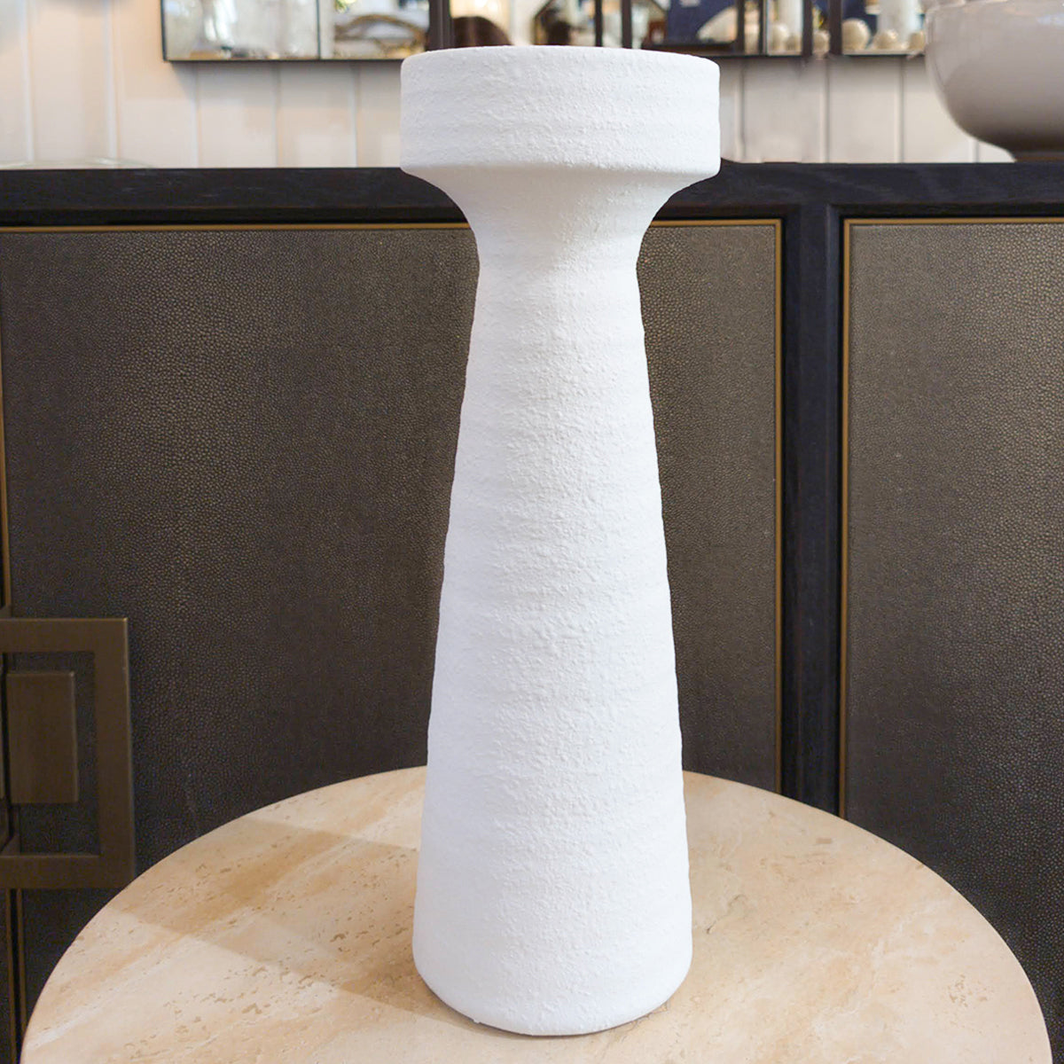 A white terracotta plaster look candleholder with a textured finish, displayed on a wooden surface with a dark background.