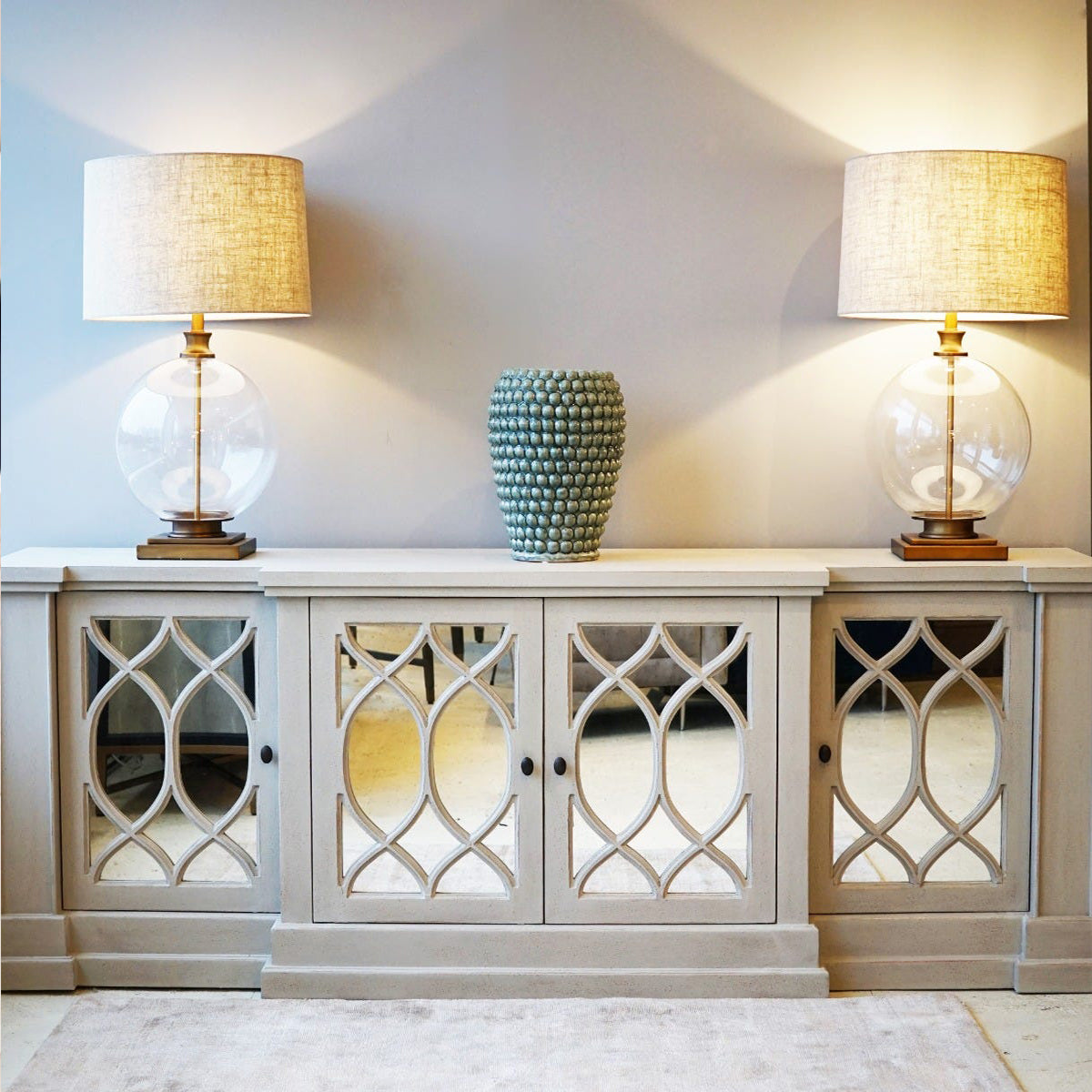 Decorative cabinet with glass doors featuring intricate patterns, and two table lamps with glass bases.