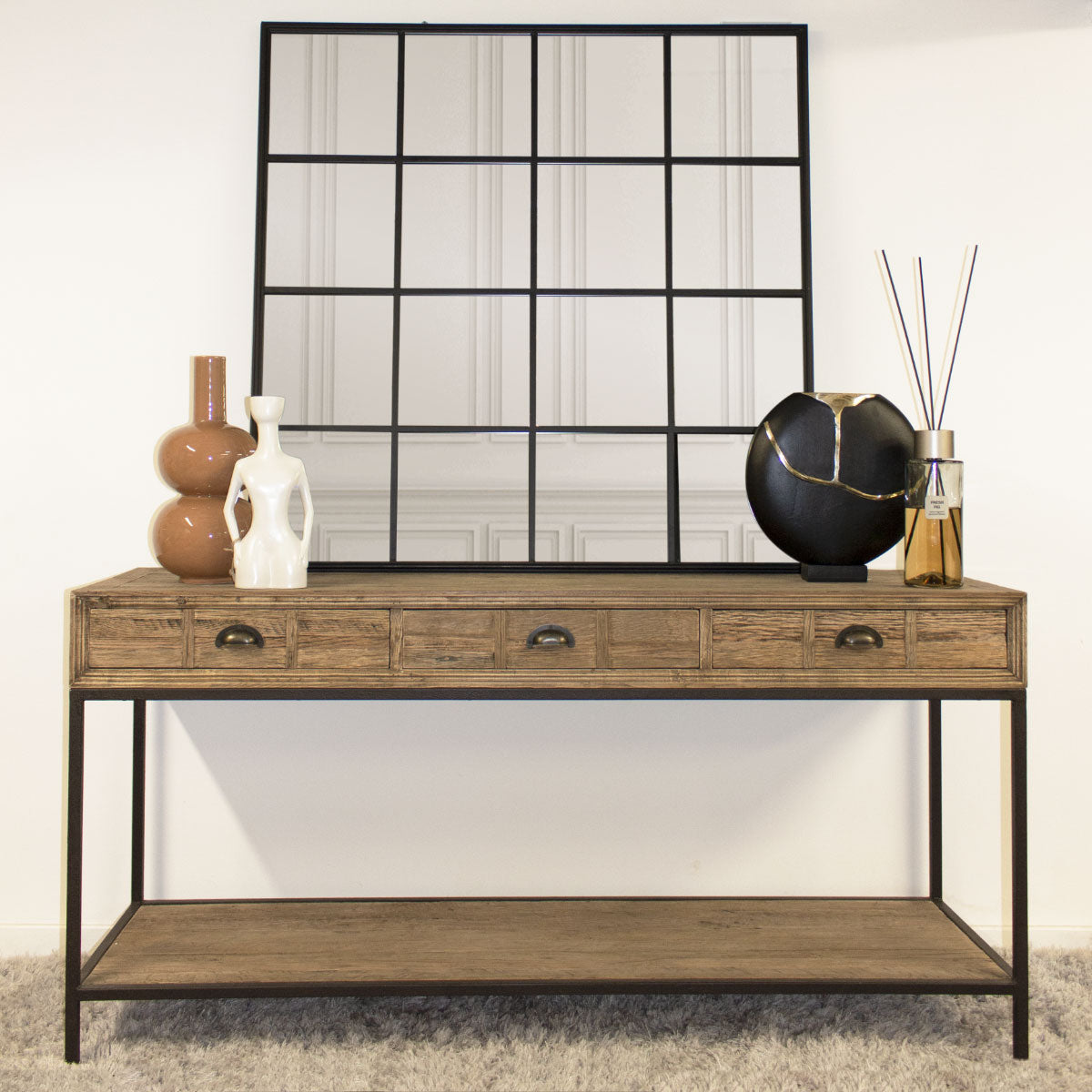 Wooden console table with decorative items against a wall with a large black grid mirror.