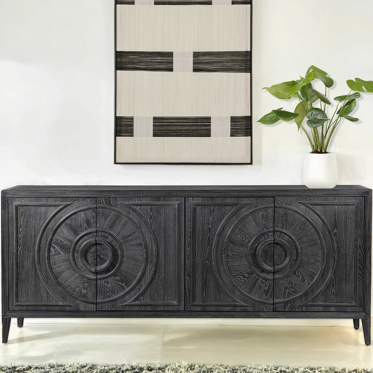 Dark wooden sideboard with decorative carvings in a room with a plant and abstract art.